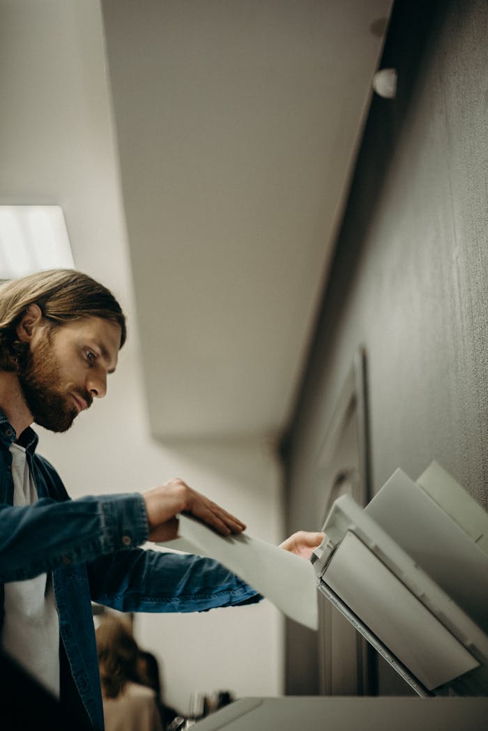 A man operates a printer in a modern office setting, emphasizing professional workflow.